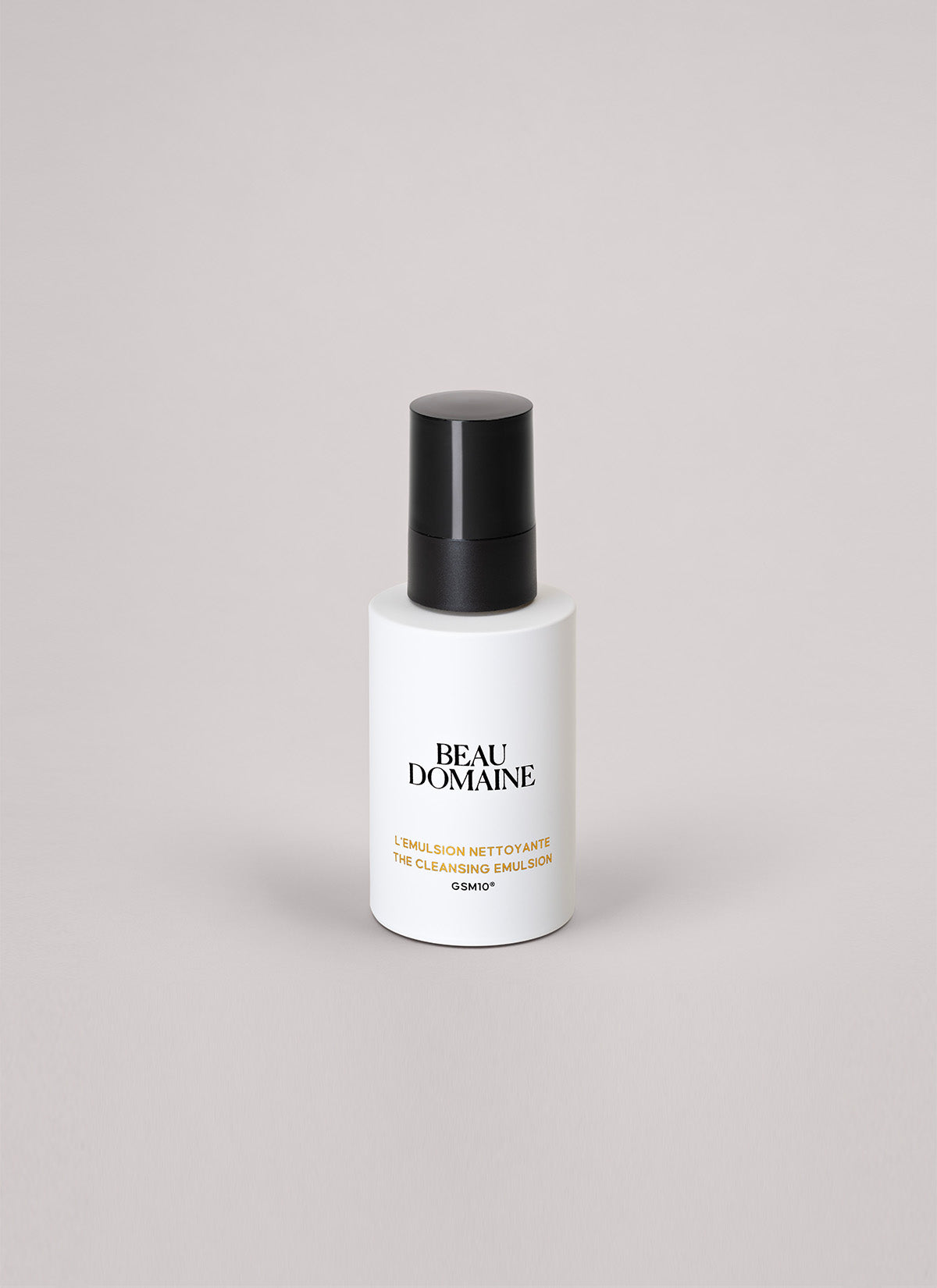 Flacon blanc The Cleansing Emimsop avec bouchon noir portant la mention « Beau Domaine » sur un fond gris clair