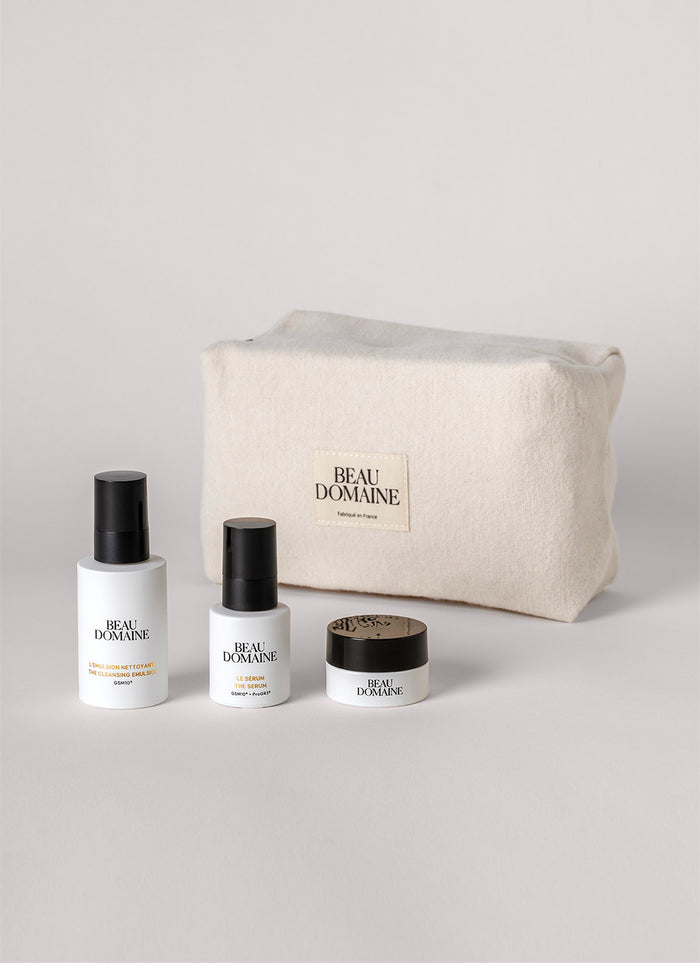 Coffret cosmétique avec flacons et un pot devant une pochette 'Beau Domaine' sur fond gris clair